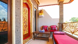 A balcony with a red bed, two chairs, a table, and a decorative door. - Jungut Guest House By Zuzu (Ubud)