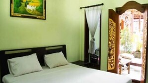 A room with a bed, a painting on the wall, a curtain, and a door leading to an outdoor area. - Jungut Guest House By Zuzu (Ubud)