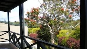 Ein überdachter Außenbereich mit Tisch und Stühlen, mit Blick auf einen Garten mit verschiedenen Pflanzen und einem Baum mit rosa Blüten.