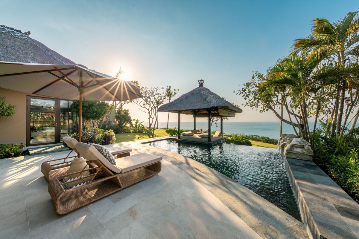 A poolside area with lounge chairs, a thatched gazebo, and a view of the sea.