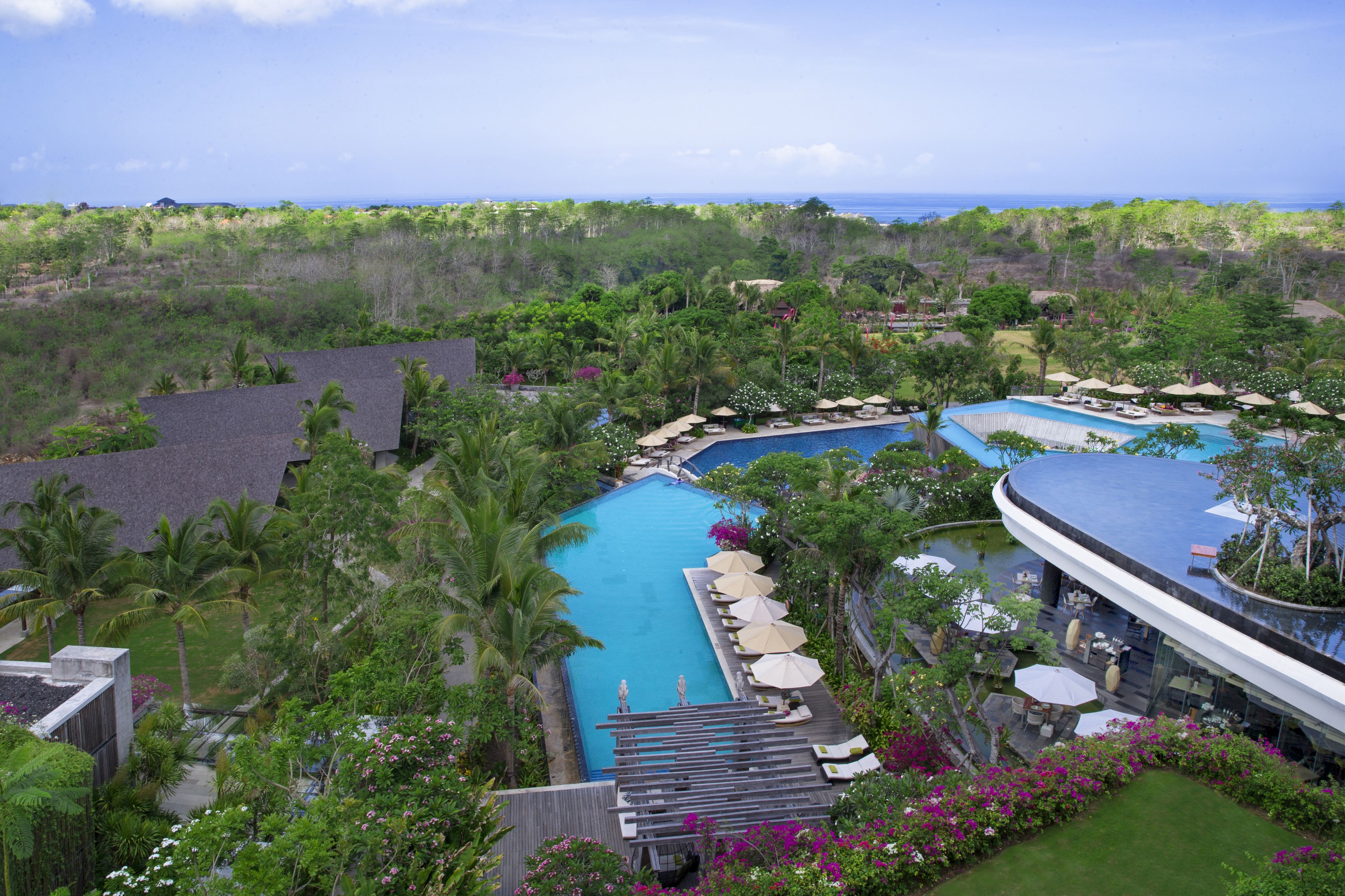 A resort with a large swimming pool, lush greenery, and a view of the ocean.