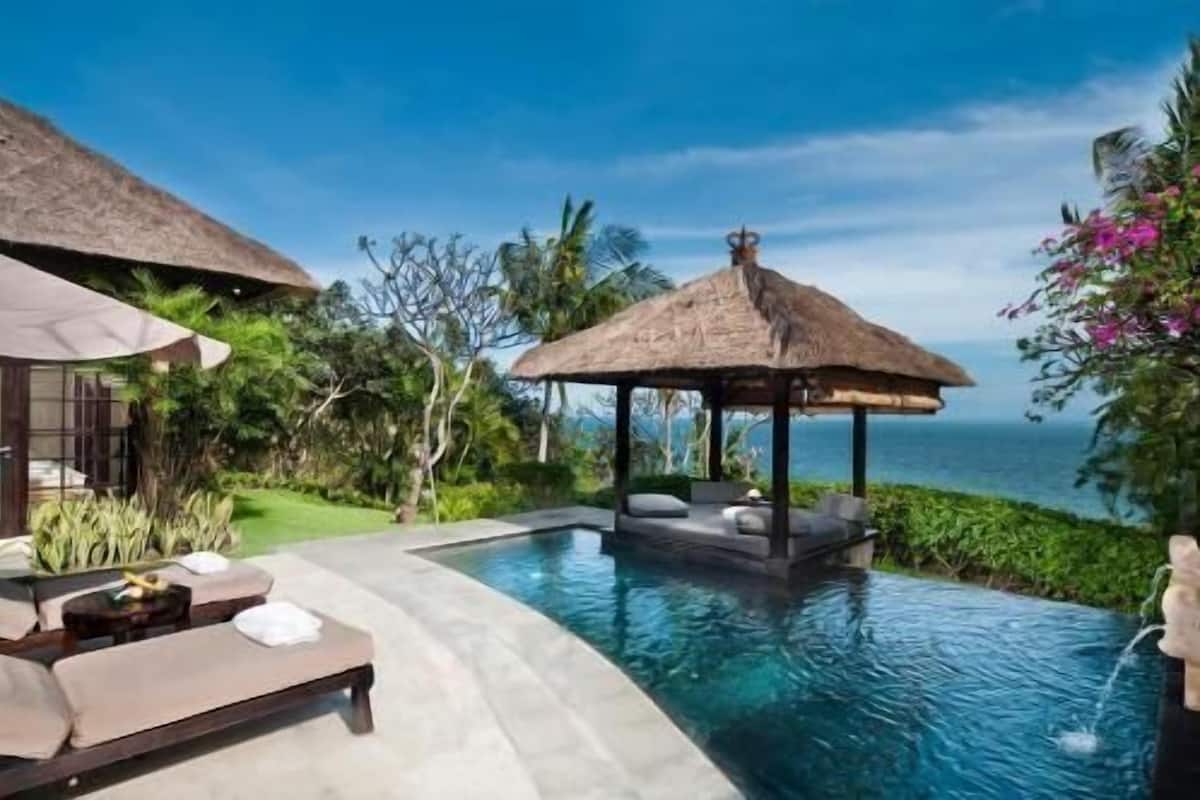 A poolside area with a lounge chair, a thatched-roof structure, and a view of the ocean.