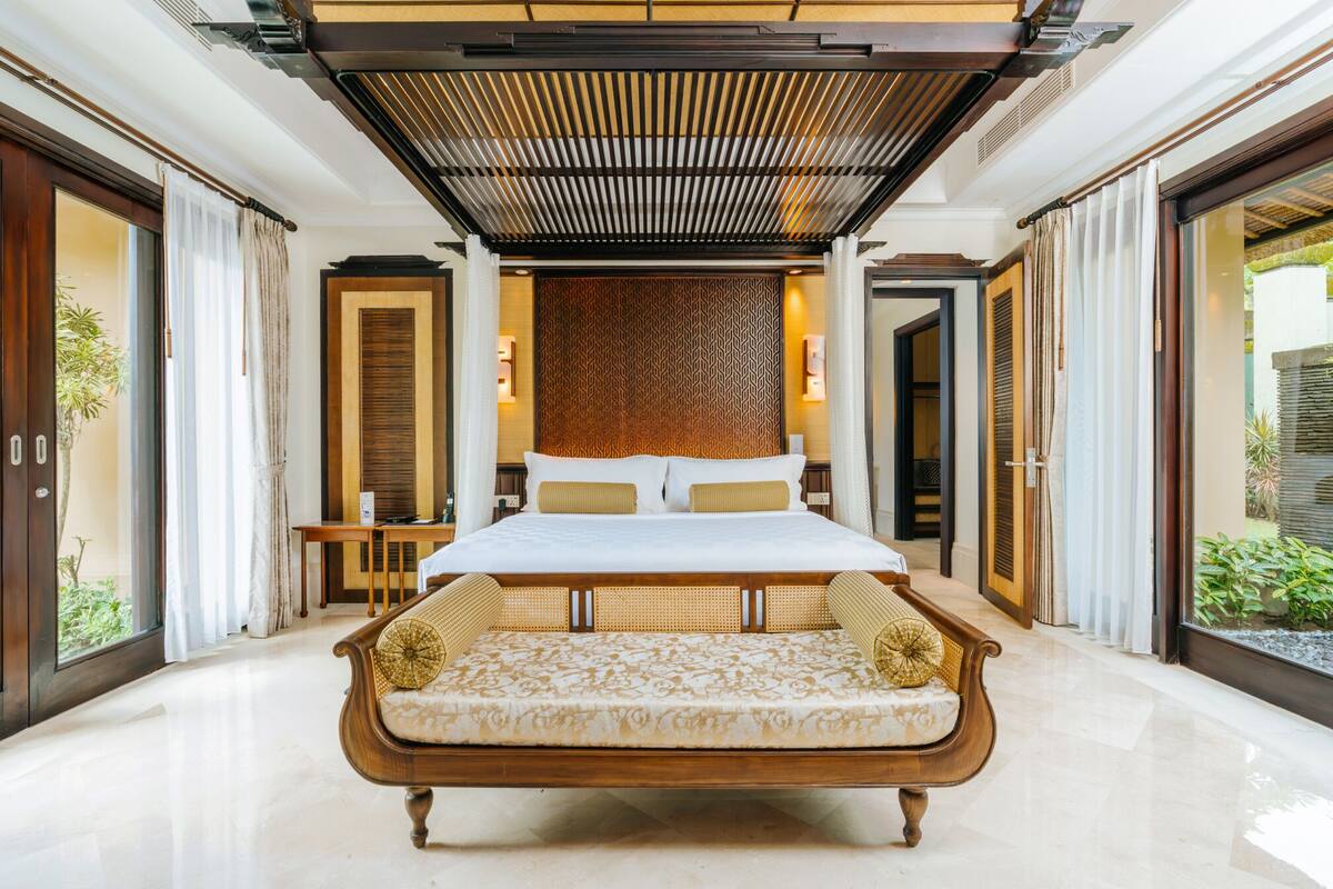 A spacious bedroom with a large bed, a bench, and a patterned wall.