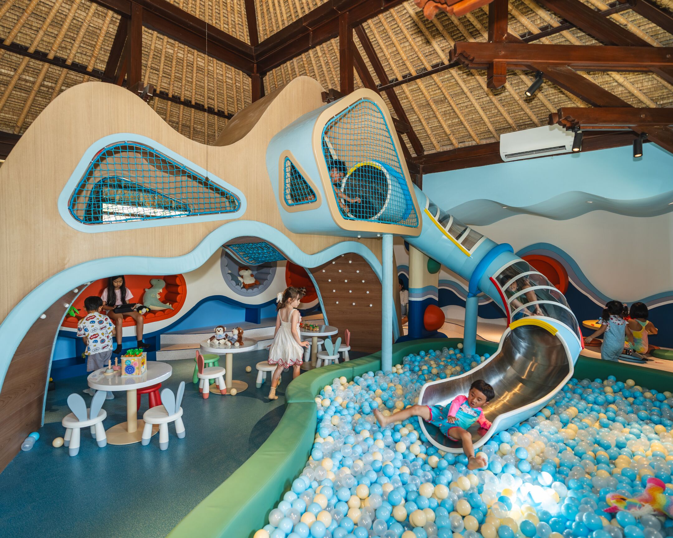 Un espace de jeux pour enfants avec un toboggan, une piscine à balles et un coin salon.