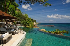 A poolside area with lounge chairs and a view of the ocean. - AYANA Villas Bali (Jimbaran)
