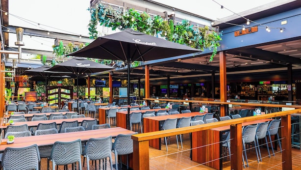 An outdoor cafe with multiple tables and chairs, umbrellas, and greenery overhead. - Park Beach Hotel Motel (Coffs Harbour)