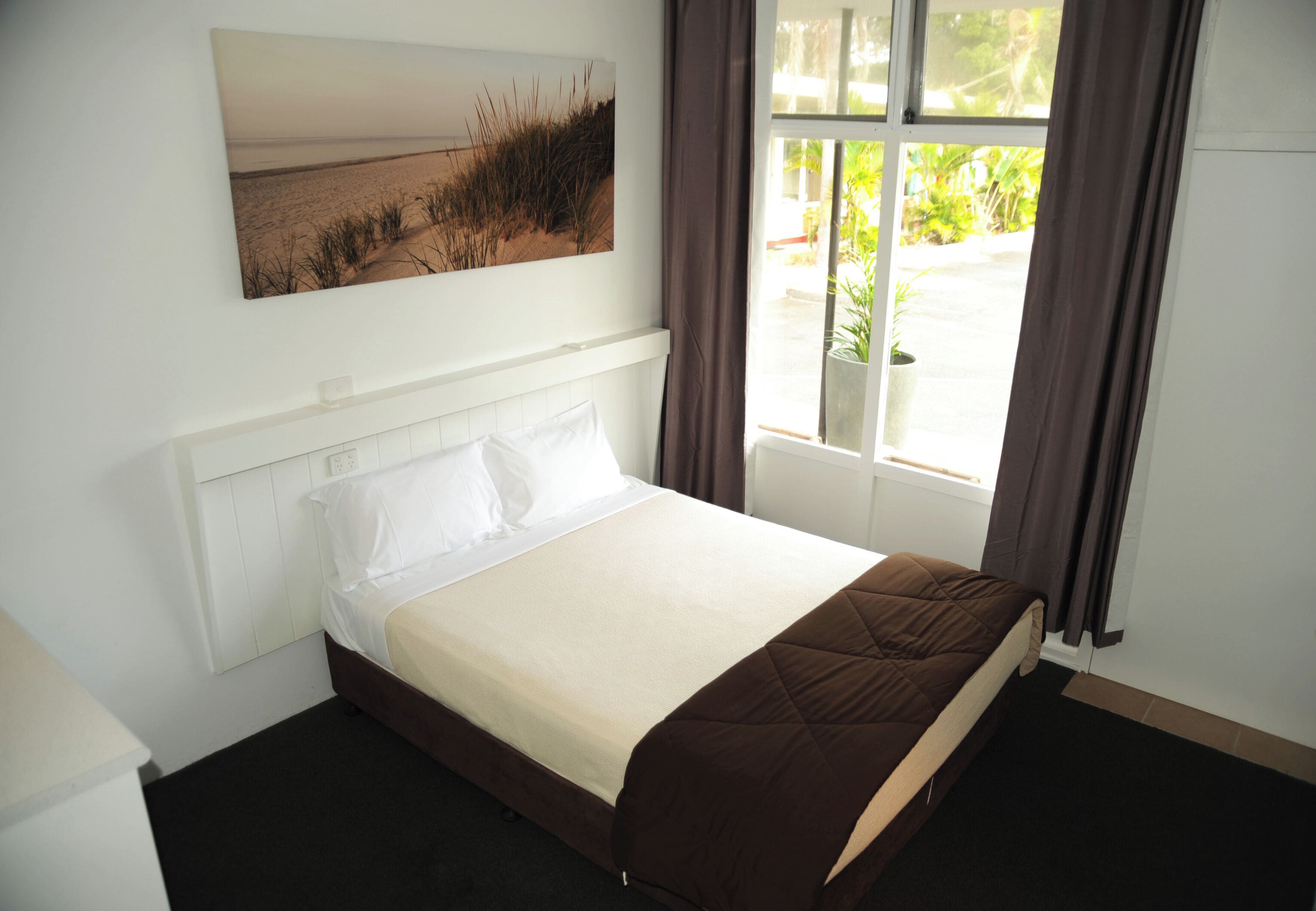 Un dormitorio con cama, ventana con cortinas y un cuadro en la pared.