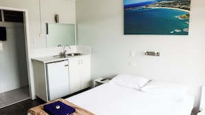 A hotel room with a bed, a small kitchenette, a bathroom, and a painting of a coastal landscape. - Park Beach Hotel Motel (Coffs Harbour)