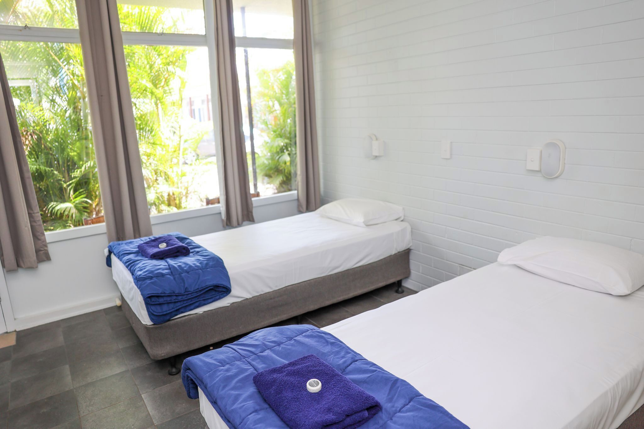 Ein Zimmer mit zwei Betten, einem Vorhangfenster und Blick auf Grünfläche.