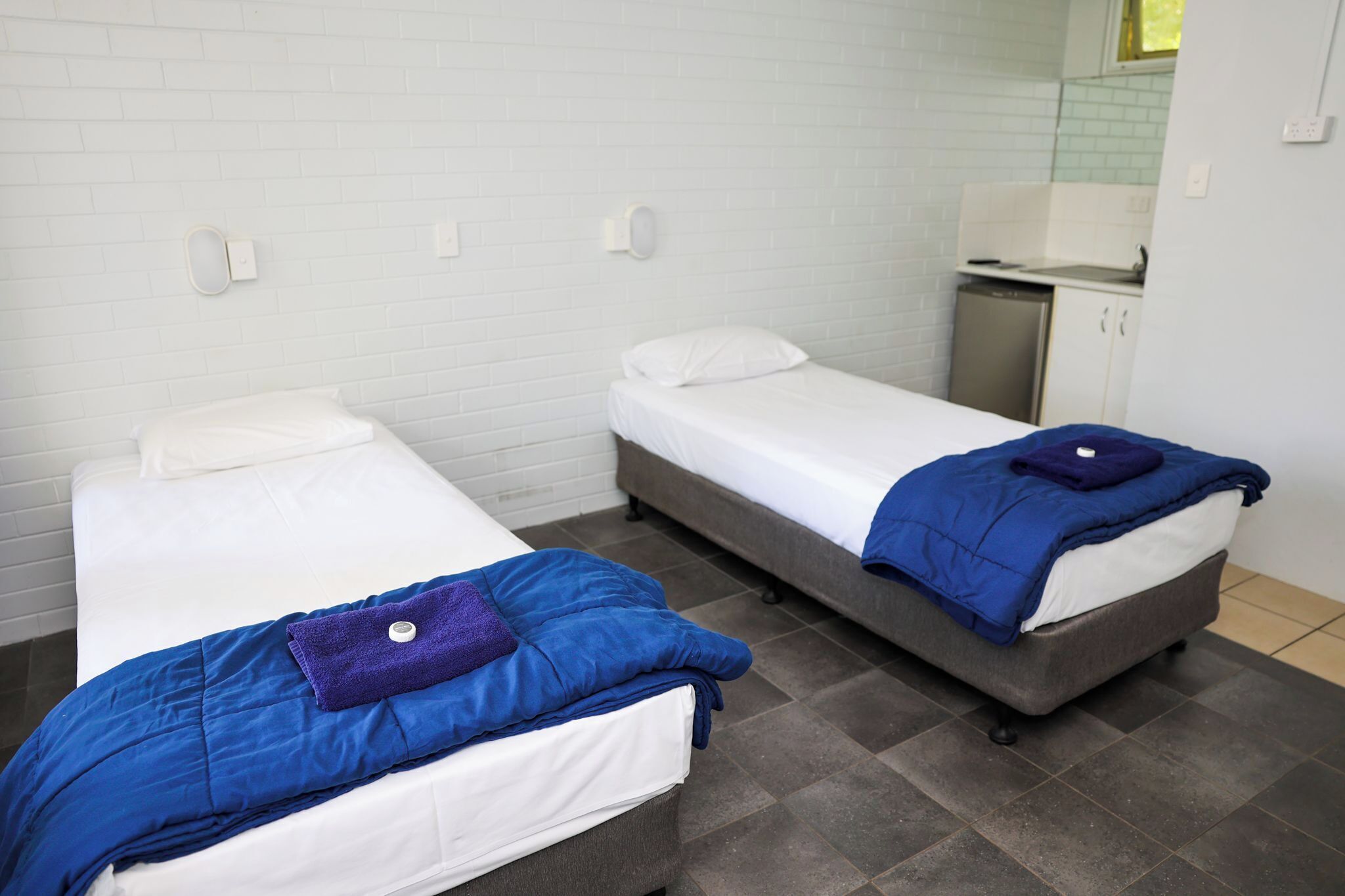 Een kamer met twee eenpersoonsbedden, elk met een blauwe deken en een wit kussen.