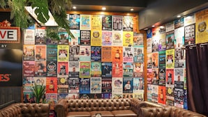 A cozy lounge area with a brown leather sofa and a small table, surrounded by a wall covered with colorful event posters. - Park Beach Hotel Motel (Coffs Harbour)