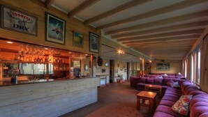 Un espace bar avec un comptoir en bois et diverses bouteilles, un coin salon avec des canapés violets et des tableaux encadrés aux murs.