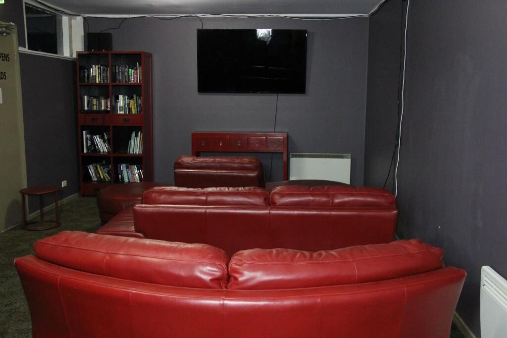 A room with a red leather couch, a bookshelf, and a flat-screen TV mounted on the wall.