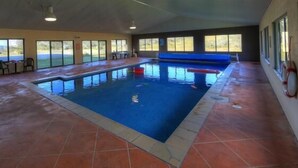 Une piscine intérieure avec de grandes baies vitrées offrant une vue dégagée, un bord de piscine bleu et un sol carrelé.