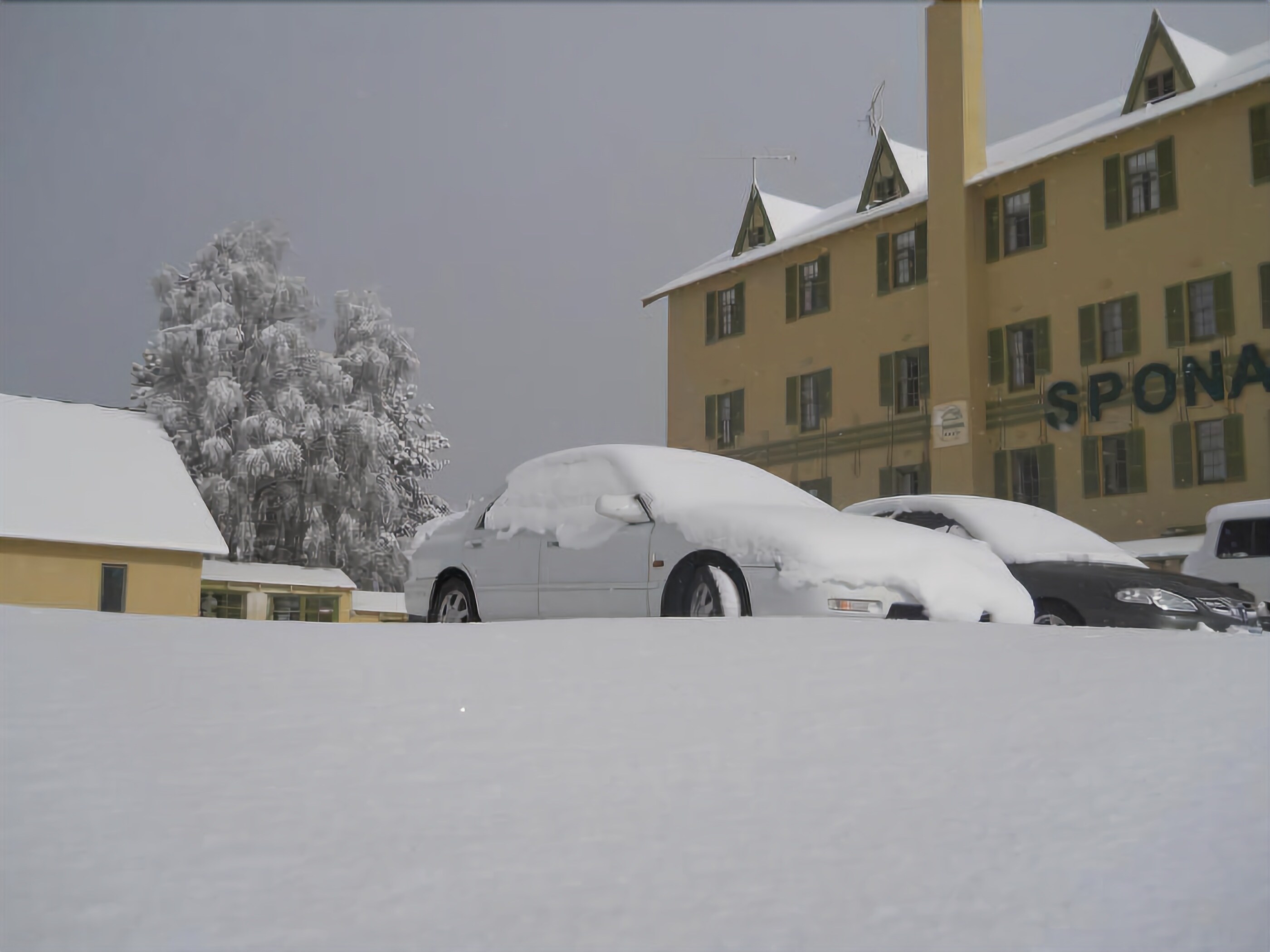 A building with the sign "SPON" partially visible, surrounded by snow-covered cars.