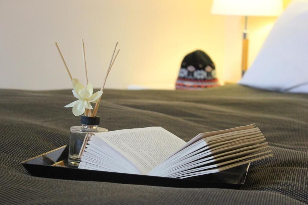 A book on a tray, a small vase with reeds, and a lamp in the background.
