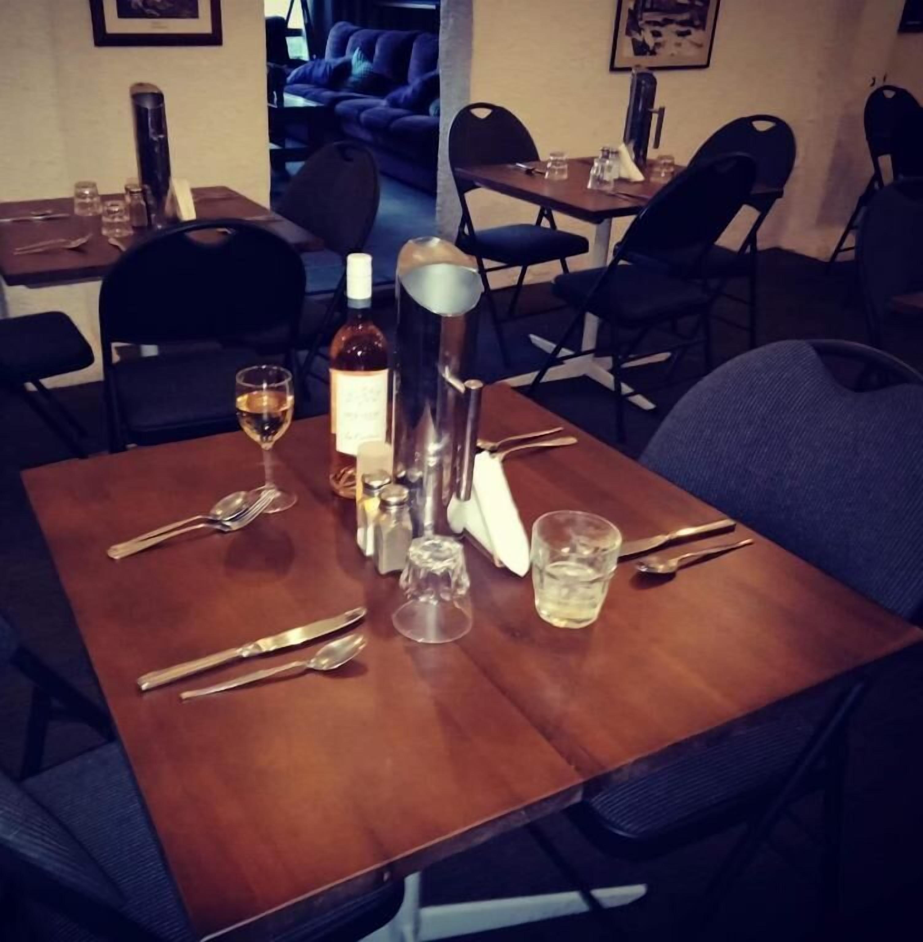 Uma mesa de jantar posta com talheres, uma garrafa de vinho, copos e uma garrafa de água.