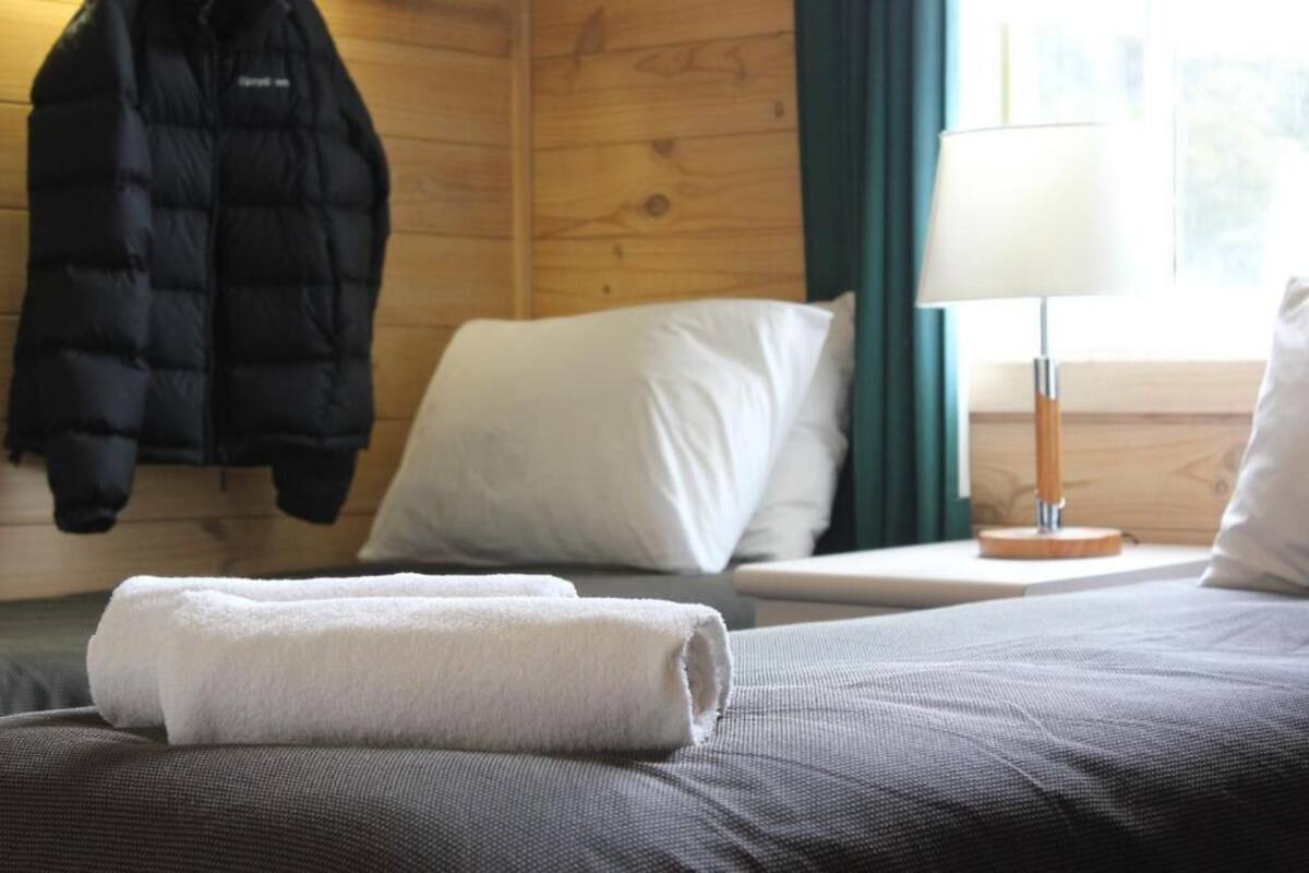 Una habitación de hotel con una cama, una mesita de noche, una lámpara y un abrigo colgado en la pared.