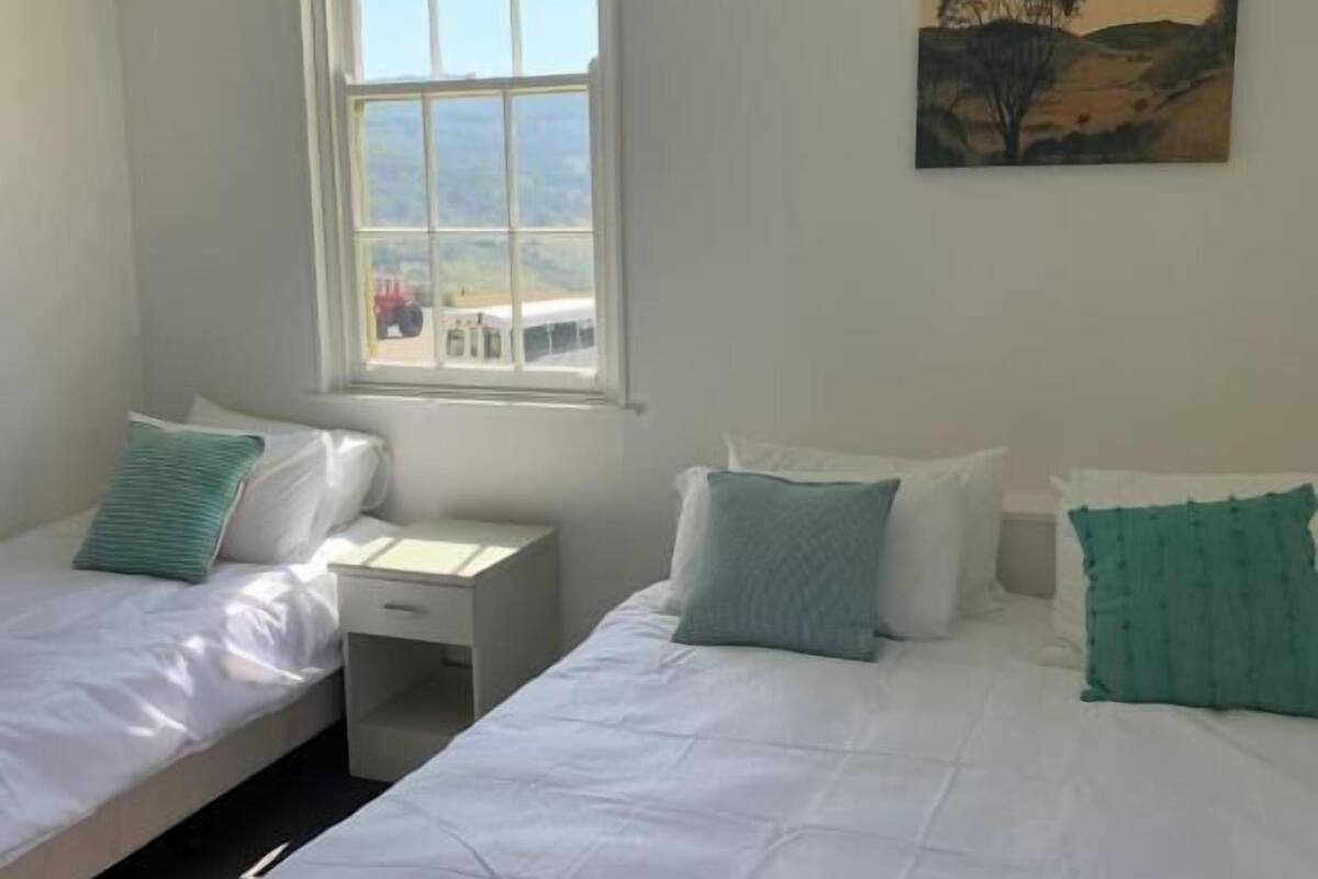 Una habitación con dos camas individuales, una mesita de noche pequeña, una ventana con vistas al paisaje y un cuadro en la pared.