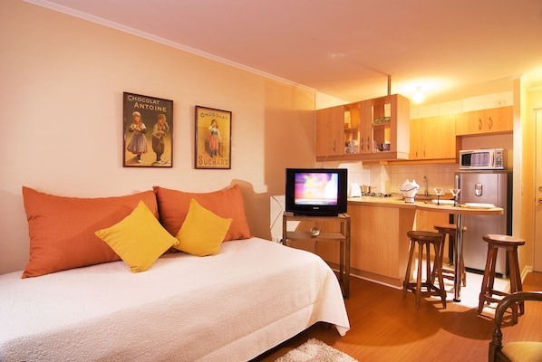 Un dormitorio con cama, televisor y kitchenette con microondas.