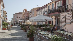 A cobblestone street lined with outdoor cafes, featuring tables and chairs, potted plants, and buildings with balconies and railings. - Residence La Reggia di Nausicaa (Santa Teresa di Gallura)