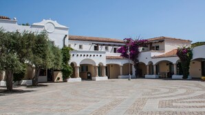 A courtyard with a tiled floor, white buildings, and arched doorways. - Residence La Reggia di Nausicaa (Santa Teresa di Gallura)
