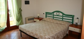 A bedroom with a bed, two bedside tables, a nightstand, a wall-mounted heater, and a window with curtains. - Residence La Reggia di Nausicaa (Santa Teresa di Gallura)