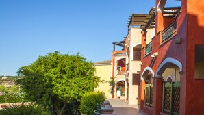 A row of traditional buildings with arched doorways and balconies, surrounded by greenery. - Residence La Reggia di Nausicaa (Santa Teresa di Gallura)