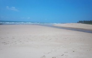 Ein weiter Sandstrand mit sanften Wellen und blauem Himmel.