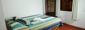 Una cama individual con colcha a rayas y dos almohadas, una silla de madera y una ventana con cortinas.