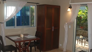 A room with a bed, a table with chairs, a wardrobe, a window with curtains, and a door leading to an outdoor area. - E&J Boutique Residences (Sosúa)