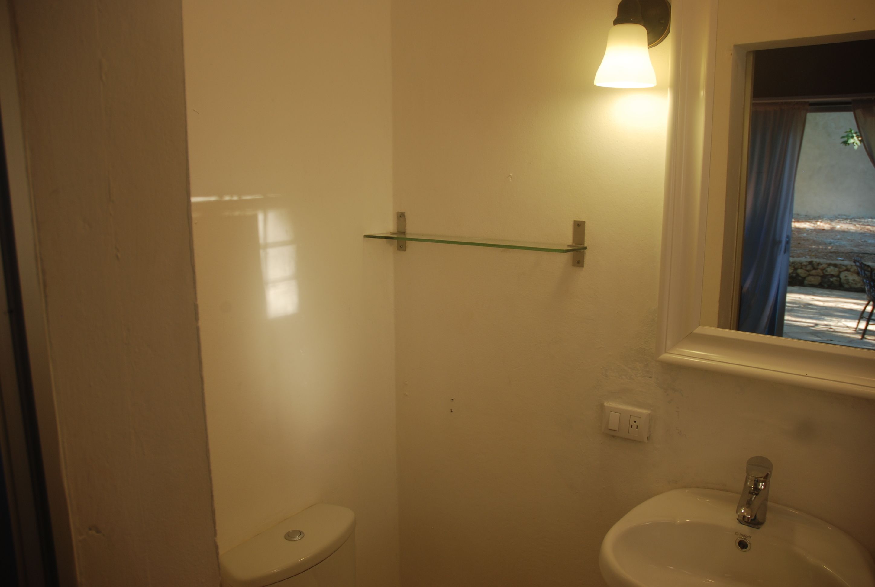 A bathroom with a toilet, a sink, a glass shelf, and a window with curtains.