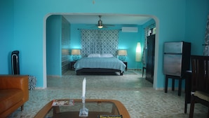 A room with a bed, a coffee table with magazines, a TV, and a refrigerator. - E&J Boutique Residences (Sosúa)