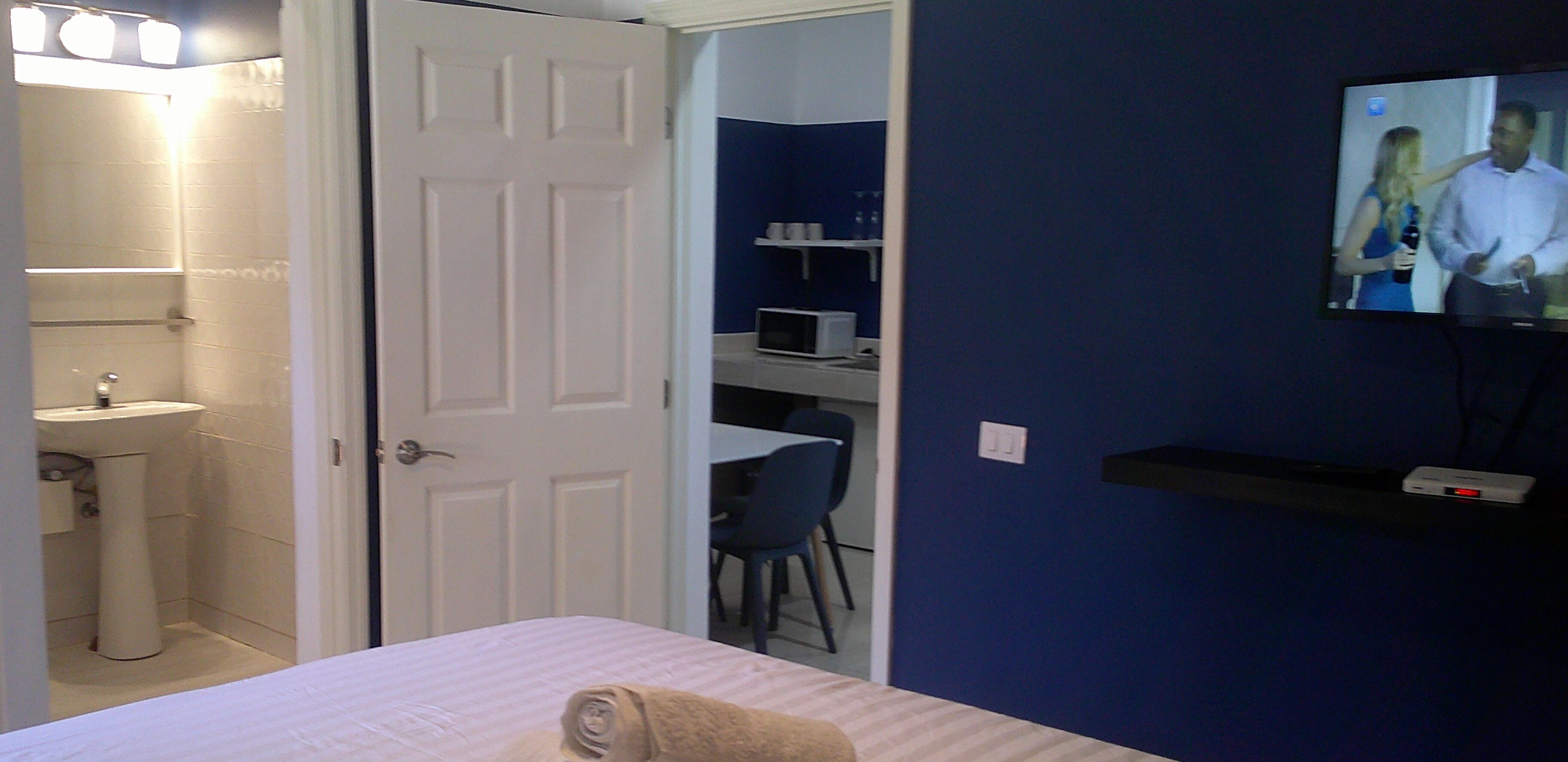 A hotel room with a bed, a bathroom with a sink, a TV mounted on the wall, and a desk with a chair.