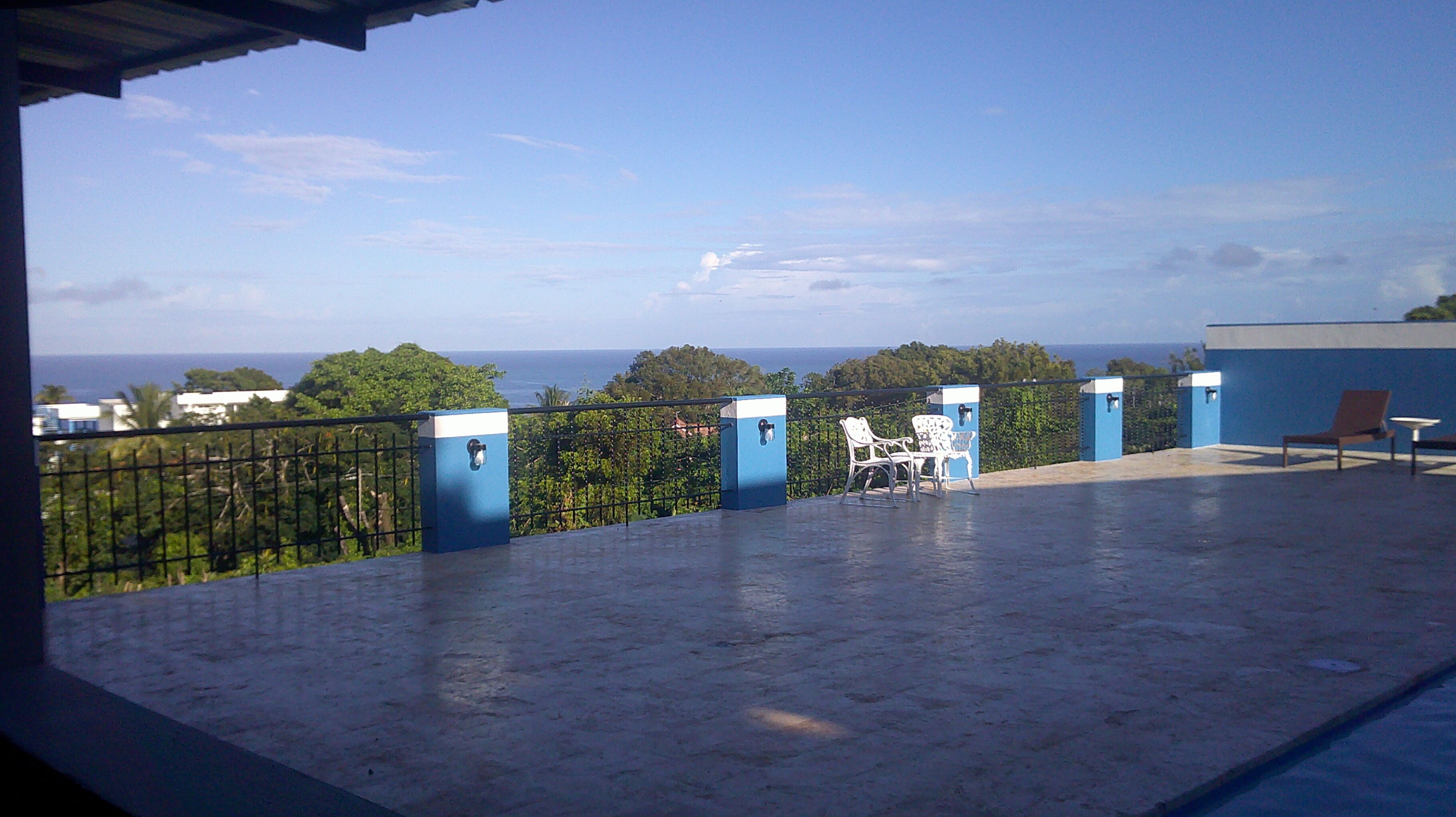 A balcony with a view of the ocean, a blue railing, and a white chair.