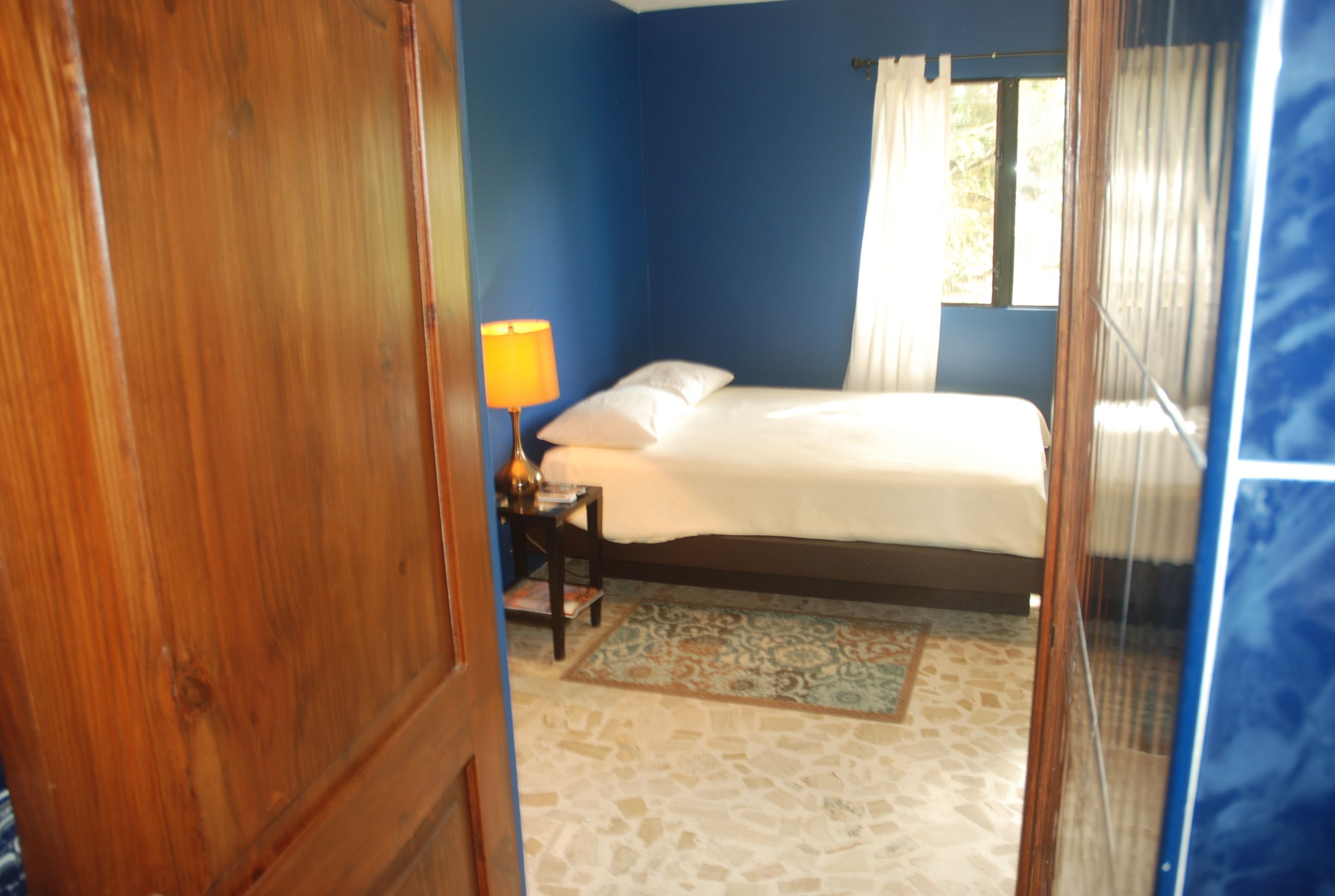 A bedroom with a bed, a nightstand, a lamp, and a window with curtains.