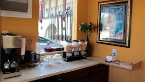 A coffee station with a coffee maker, cups, and a sugar dispenser. - Executive Inn and Suites (Goliad)