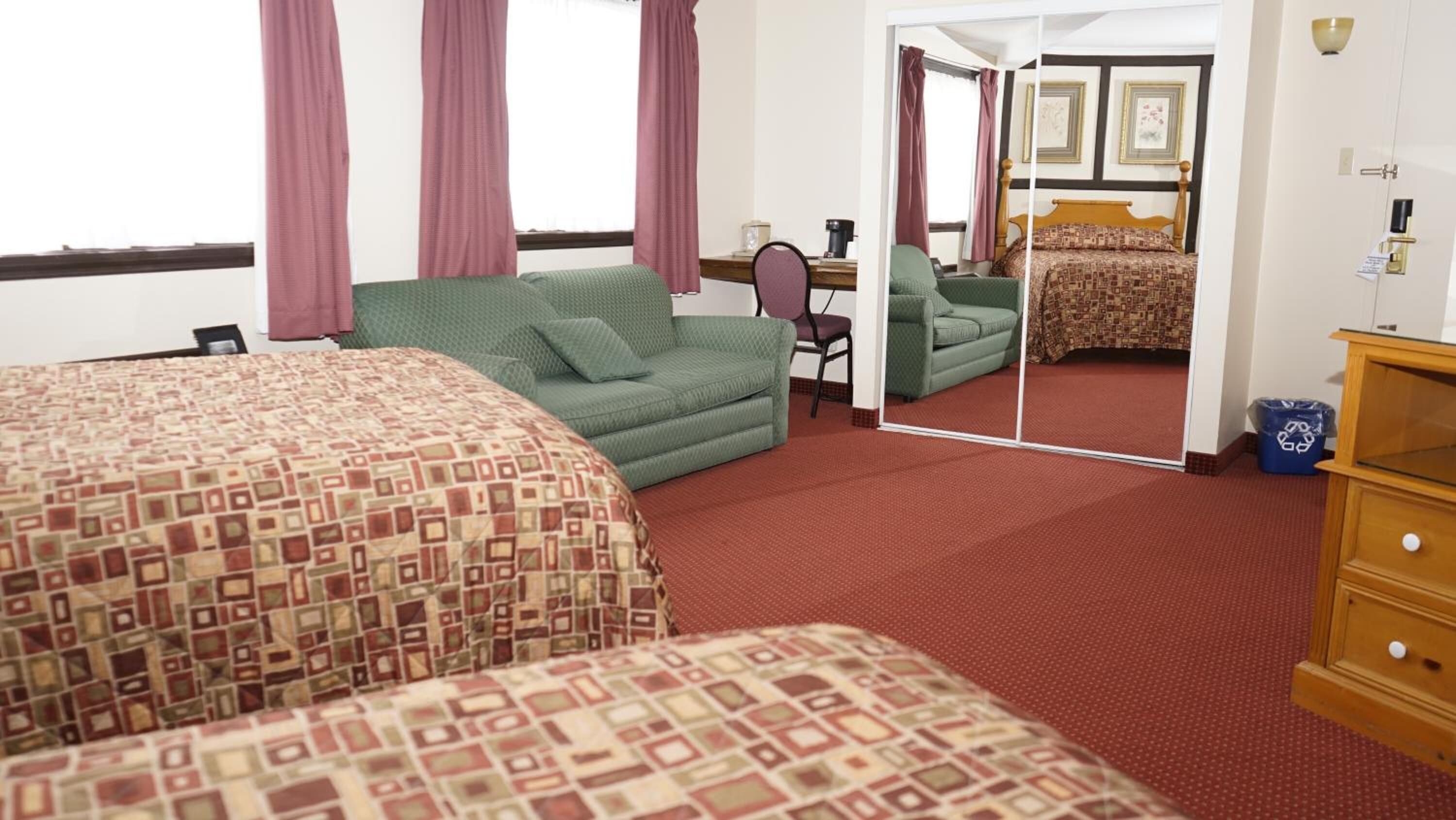 A hotel room with a large bed, a green sofa, a small desk with a chair, and a mirror reflecting the room.