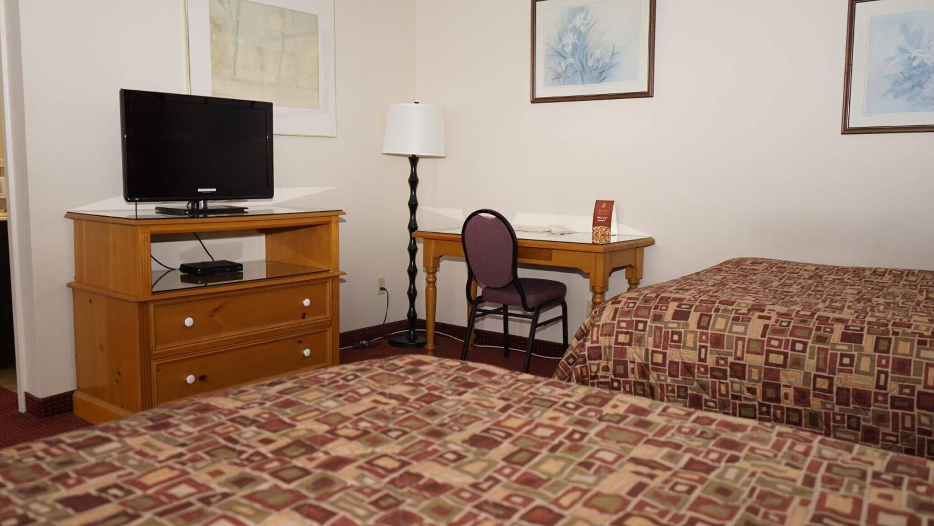Een hotelkamer met twee bedden, een bureau met stoel, een televisie op een dressoir en kunstwerken in lijsten aan de muur.