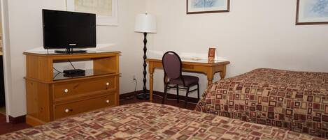 Habitación de hotel con dos camas, un escritorio con silla, un televisor en una cómoda y obras de arte enmarcadas en las paredes.