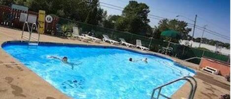 Una piscina con persone che nuotano, circondata da sdraio e una recinzione.