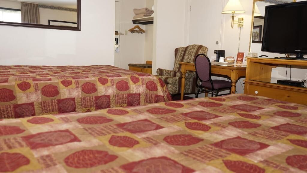 Une chambre d’hôtel avec deux lits, un bureau, une chaise, une télévision et un miroir.