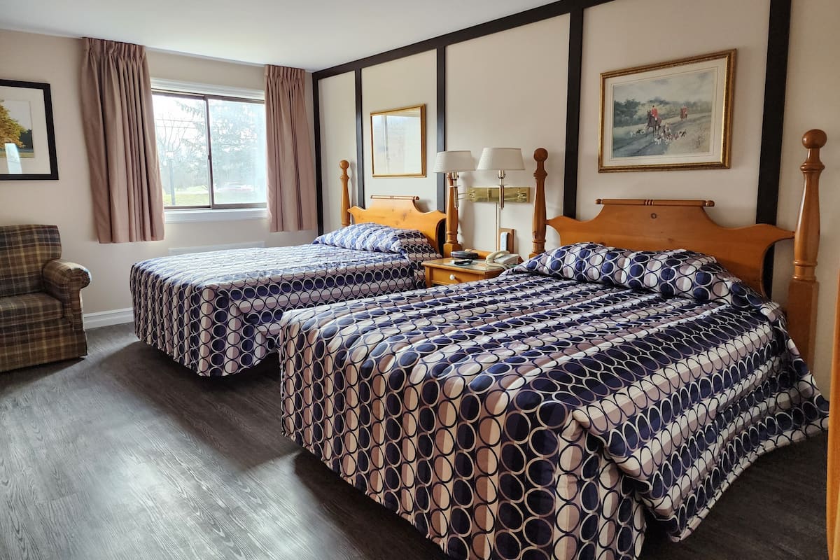 Een hotelkamer met twee bedden, een houten hoofdbord, een nachtkastje met lampen, een stoel en een raam met gordijnen.