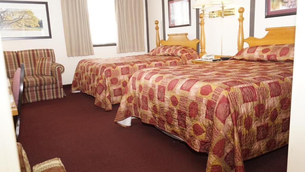 A hotel room with two beds, a chair, and a nightstand.