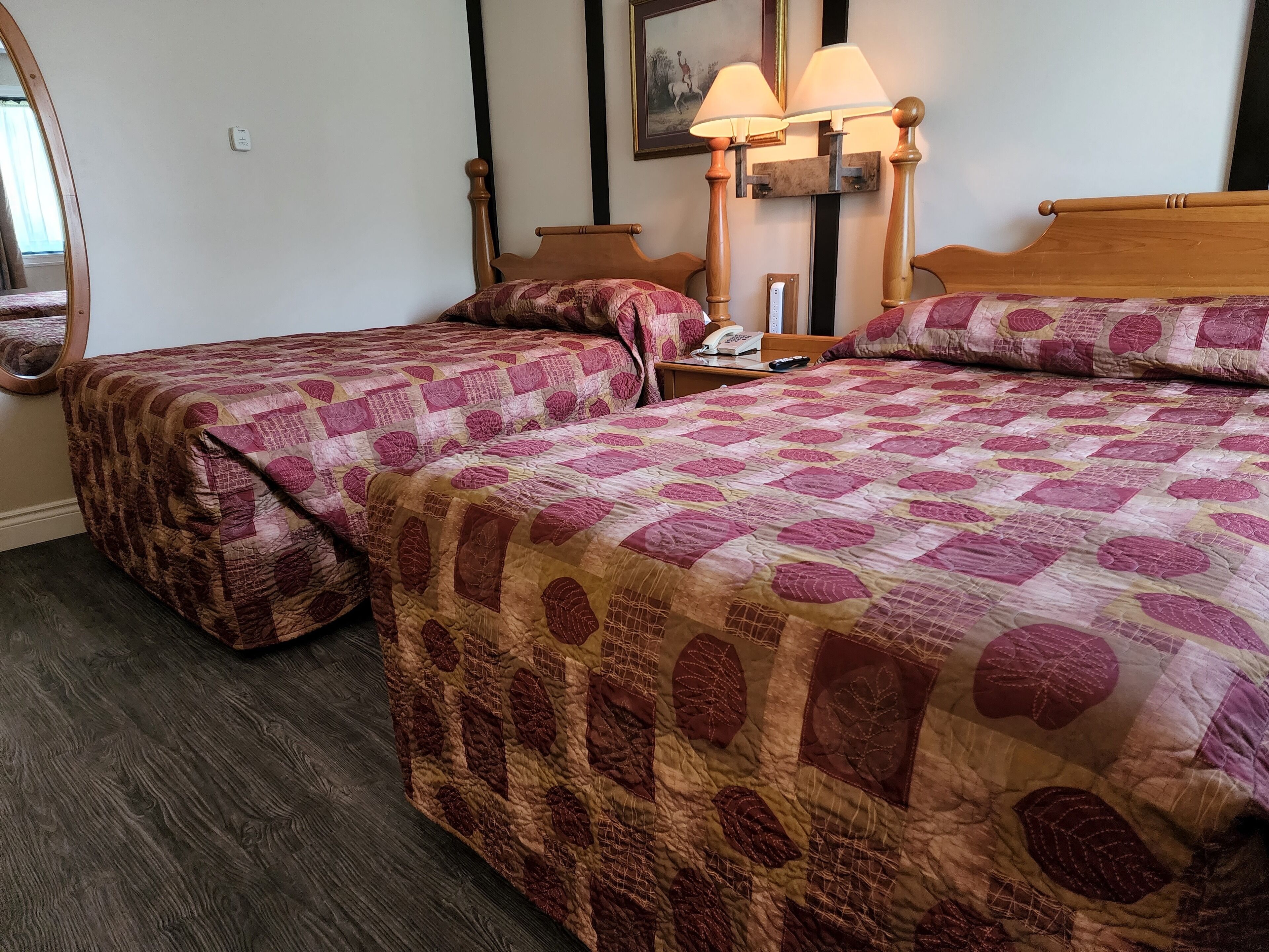 A hotel room with two beds, a wooden headboard, a nightstand with a lamp, and a mirror.