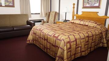A hotel room with a large bed, a sofa, a chair, a nightstand, and a lamp.