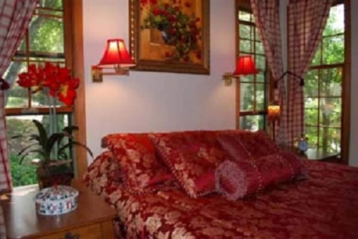 A bedroom with a floral bedspread, a nightstand with a lamp, and a window with curtains.