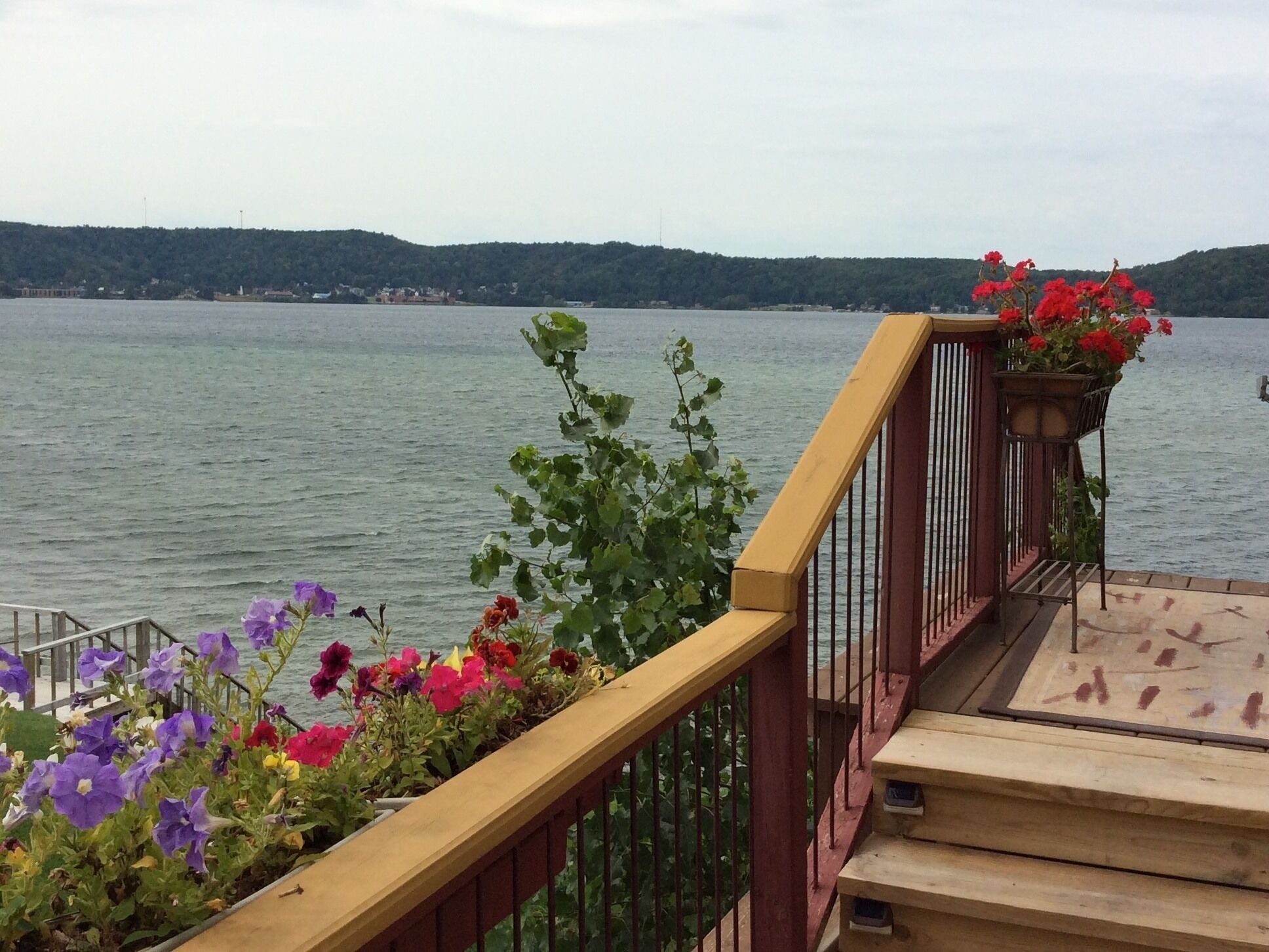 Une terrasse en bois dotée d’une balustrade, d’où l’on peut admirer un plan d’eau et une colline au loin.
