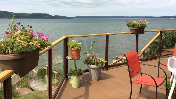 A deck with potted plants, a red chair, and a view of a lake. - Pictured Rocks Bed And Breakfast (Munising)