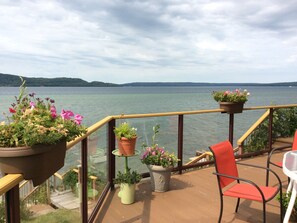 A deck with potted plants, a red chair, and a view of a lake.